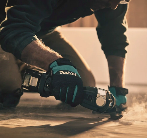 Hantverkare i Makita-handskar som sågar i ett trägolv med ett batteridrivet multiverktyg, KiwiTools